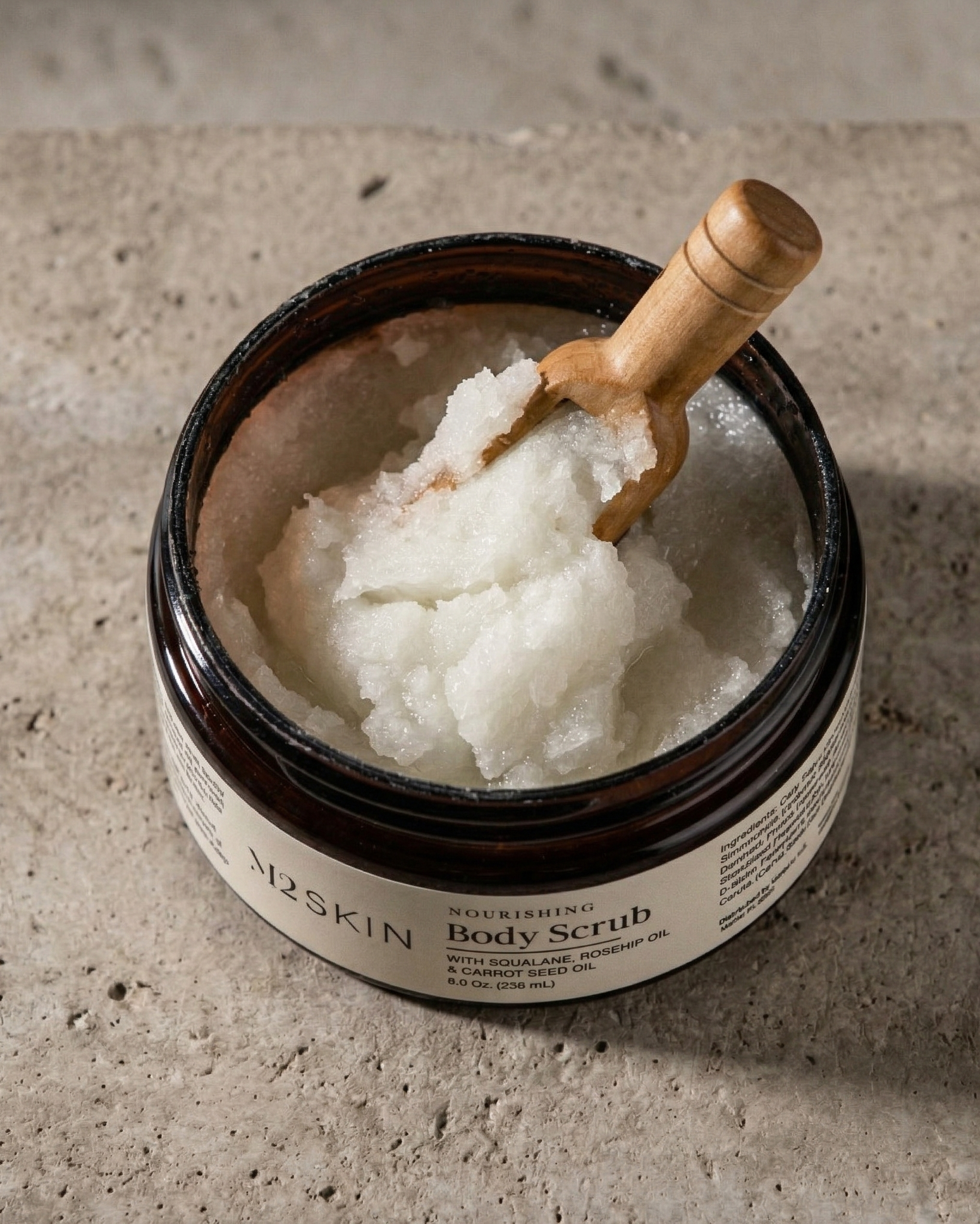 Jar of body scrub with a wooden scoop on a concrete surface